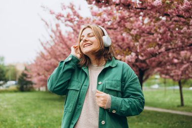 Parkta müzik dinleyen 30 'lu yaşlarda, kocaman kulaklıklı çekici bir kadının portresi. Müzik aşığı müziğin tadını çıkarıyor. Sakura 'nın çiçek açan bir dalıyla bahar arkaplanı.