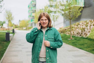 Binanın dışında cep telefonuyla yürüyen kızgın bir kadın. Hüsrana uğramış bir kadın telefonda konuşuyor. Yaz zamanı..