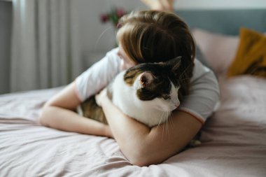 Evde kedisi olan mutlu genç bir kadın. Soğuk havada, evcil hayvan dostu ve bakım konsepti. Sokak kedisi yatakta uyuyor. Rahat ev arka planı, sabah yatma zamanı.