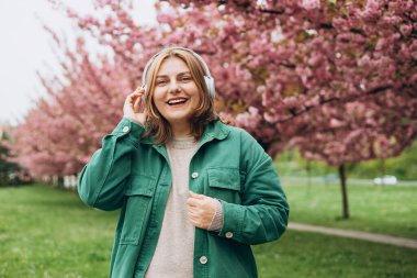Parkta müzik dinleyen 30 'lu yaşlarda, kocaman kulaklıklı çekici bir kadının portresi. Müzik aşığı müziğin tadını çıkarıyor. Sakura 'nın çiçek açan bir dalıyla bahar arkaplanı.