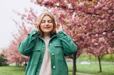 Parkta müzik dinleyen 30 'lu yaşlarda, kocaman kulaklıklı çekici bir kadının portresi. Müzik aşığı müziğin tadını çıkarıyor. Sakura 'nın çiçek açan bir dalıyla bahar arkaplanı.
