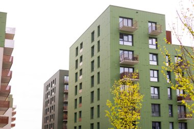 Güneşli bir yaz gününde modern apartman binaları. Modern apartman kompleksinin yeşil cephesi. Balkonlu ev cephesi.