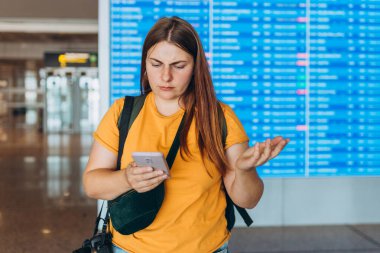 Kafası karışmış 30 'lu yaşlarda cep telefonu tutan, internetten bilgi panosunun yanındaki Trip Varış Yeri' ni kontrol eden bir kadın. Gecikmeli uçuş. Şok edici derecede kötü haberler alıyor.