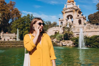 Moda sektöründe güzel bir kadın akıllı telefon kullanarak sokaklarda zaman geçirir. Barcelona 'daki Ciutadella Park' ında cep telefonuyla konuşan mutlu kız.