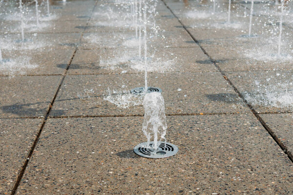 Water droplets spread from the fountain in the air. Splashing water from a fountain in the park