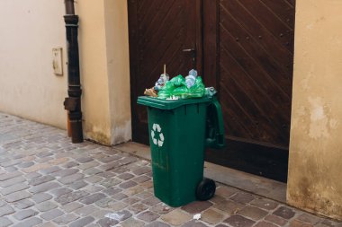 Yolun kenarındaki çöp yığını. Plastik yeşil tekerlekli çöp geri dönüşüm çöpü çöp toplama için yolun yanında. Ekoloji kavramı.