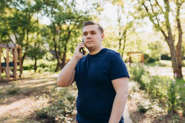 Şehir parkında 30 'lu yaşlardaki mutlu sarışın adam akıllı telefondan konuşuyor.