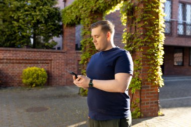 Sokakta akıllı telefon kullanan 30 'lu yaşlarda, kendine güvenen genç bir adam. İletişim ve cihazlar, bağlantı konsepti. Dışarıda dinlenirken cep telefonu tutan bir adam.