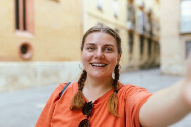 Şehirde yürürken selfie çeken gülümseyen genç bir kadın. Sosyal medya uygulamasında paylaşmak için dışarıda poz veren pozitif neşeli kız öğrenci