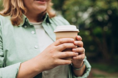 Sonbahar parkında kahve. Yemek, dinlenme, paket konsepti. Logoyu kupanın üzerine yerleştir, maket yap. Park arka planında kahverengi kağıt bardak tutan kadın..