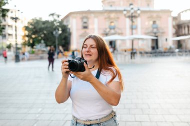 Kameralı mutlu kızıl saçlı kadın fotoğrafçı dışarıda fotoğraf çekiyor. Valencia 'da turizm. Gezgin kız Valencia 'yı ziyaret ediyor. İspanya 'da tatiller.