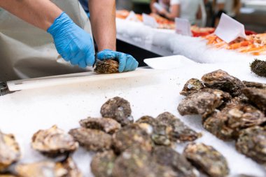 İçi boş ve yassı istiridyeleri açıyorum. İstiridye ve istiridye açma süreci. Erkek eller açık deniz kabukları müşteri için, balık pazarı.