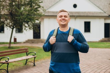 Gülümseyen mutlu genç adam yeşil şehir parkında dinleniyor. 30 'lu yaşlarda, kendine güvenen bir adam..