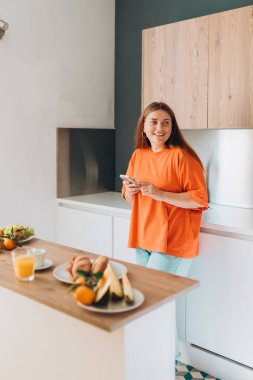 Mutfakta elinde cep telefonu olan mutlu 30 'lu yaşlarda bir kadın. Ev hayatı ve boş zaman anları. Yüksek kalite fotoğraf