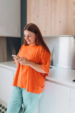 Mutfakta elinde cep telefonu olan mutlu 30 'lu yaşlarda bir kadın. Ev hayatı ve boş zaman anları. Yüksek kalite fotoğraf