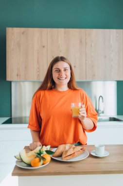 Mutfakta elinde bir bardak portakal suyu tutan mutlu 30 'lu yaşlarda bir kadın. Ev hayatı ve boş zaman anları. Yüksek kalite fotoğraf.