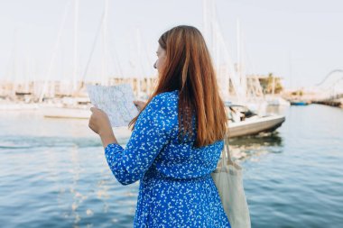 Seyahat etmek için ilginç yerleri keşfederek tatil kavramı. Yaz gününde güzel bir kadın mekânları arıyor. Haritalı bir kadın deniz kenarında yürüyor.