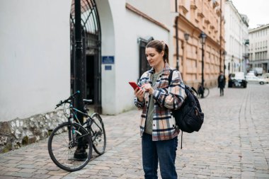 Sırt çantalı mutlu genç kadın akıllı telefonunu kontrol ediyor. Açık havada akıllı telefon kullanan 30 'lu yaşlardaki güzel bir kızın portresi. Kentsel yaşam tarzı konsepti