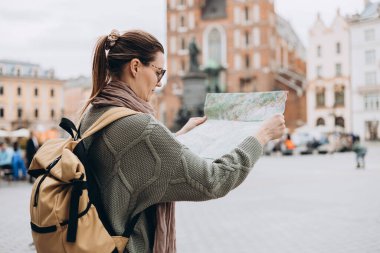 Çekici genç bayan turist yeni şehri keşfediyor. Krakow 'daki Pazar Meydanı' nda elinde kağıt harita tutan mutlu kız. Sonbaharda Avrupa 'yı geziyorum. Aziz Mary Bazilikası