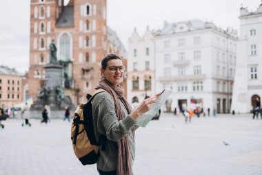 Çekici genç bayan turist yeni şehri keşfediyor. Krakow 'daki Pazar Meydanı' nda elinde kağıt harita tutan mutlu kız. Sonbaharda Avrupa 'yı geziyorum. Aziz Mary Bazilikası