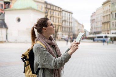 Çekici genç bayan turist yeni şehri keşfediyor. Krakow 'daki Pazar Meydanı' nda elinde kağıt harita tutan mutlu kız. Sonbaharda Avrupa 'yı gezmek