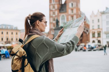 Çekici genç bayan turist yeni şehri keşfediyor. Krakow 'daki Pazar Meydanı' nda elinde kağıt harita tutan mutlu kız. Sonbaharda Avrupa 'yı geziyorum. Aziz Mary Bazilikası