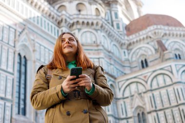 Şehir caddesinde yürüyen kadın telefonu kontrol ediyor. Floransa 'daki ünlü Duomo katedralinin yakınında akıllı telefon kullanan 30' lu yaşlardaki bir kız. İtalyan simgelerini ziyaret eden şık kadınlar. Seyahat, turizm ve tatil kavramı.