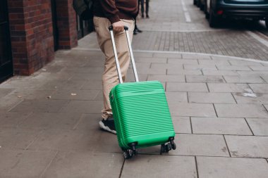 Yeşil bavulu dışarı çıkaran tanınmamış bir adam. Dikiz aynası. Uzayı kopyala Bir adam seyahat çantasıyla sokakta yürüyor..