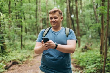 Sırt çantalı mutlu yürüyüşçü doğada dinlenirken cep telefonu kullanıyor.