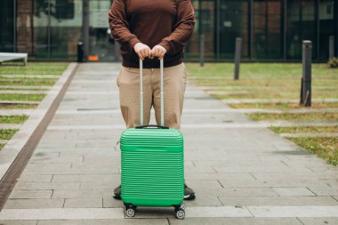 Bir bavulla gezen, şehirde gezen yüzü olmayan bir gezgin. Otelin yanındaki otobüs durağında bekleyen yolcu. El ele tutuşmaya odaklan.