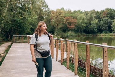 Yeşil sırt çantalı, gülen ve göl kenarında yürüyüş yapan bir kadın yürüyüşçü. Yaşam tarzı macera konsepti. 30 'ların kızı doğanın tadını çıkarıyor.