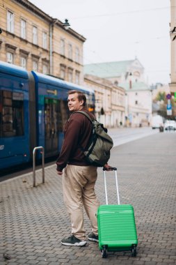 Yeşil bavulu dışarı çıkaran 30 'lu yaşlardaki mutlu adam. Dikiz aynası. Uzayı kopyala Bir adam seyahat çantasıyla sokakta yürüyor.