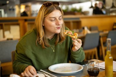 Bir kadın bir dilim pizzayı elinde tutuyor. Pizzaya odaklan. Prosciutto, jambon, roka, domates ve parmesanlı pizza. İtalyan mutfağı.