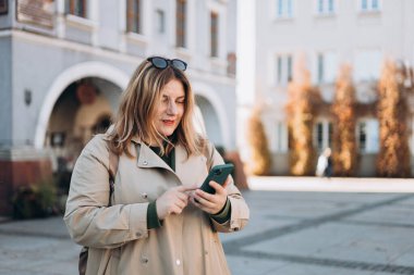 Sırt çantalı mutlu genç kadın akıllı telefonunu kontrol ediyor. Açık havada akıllı telefon kullanan 30 'lu yaşlardaki güzel bir kızın portresi. Kentsel yaşam tarzı konsepti.