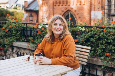 Elinde biyo-kahve fincanı tutan kadın, şehir caddesindeki kafe terasında oturuyor. Şehir konsepti. 30 'lu yılların mutlu kızı açık havada kahvesini yudumluyor.