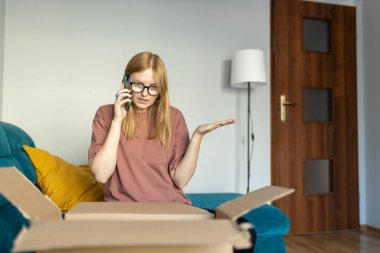 Memnun olmayan kızgın genç kadın, bozuk ürün aldıktan sonra çevrimiçi mağazayı arıyor. Müşteri kanepeye oturur, çek kutusunu alır. Kötü dağıtım hizmeti kavramı