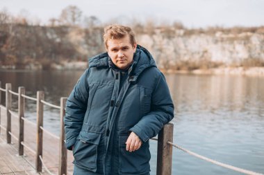 Sarışın bir adam köprüde nehre doğru yürüyor. Sonbahar geldi. Özgürlük ve aktif yaşam tarzı kavramı.