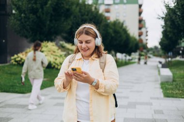 Şehir arka planında kablosuz kulaklıkla müzik dinleyen sevimli bir genç kızın yakın plan portresi. Müzik aşığı müziğin tadını çıkarıyor. Cep telefonu diktafonundan kadın sesi kaydı