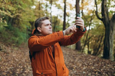 Üzgün, sinirli sarışın adam kayboldu ve ormanda tek başına yürürken telefonda internet bağlantısı bulamadı. Yolculuk, ulaşım, seyahat, teknoloji ve insan kavramı.