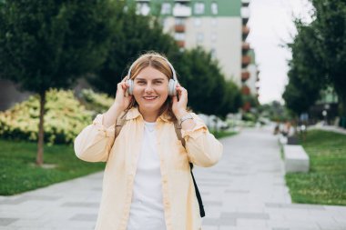 Gülümseyen 30 'lu yaşlardaki genç bir kadın şehir arka planında kablosuz kulaklıkla müzik dinliyor. Müzikten zevk alan müzik aşığı, sakin an.