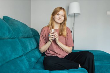 Genç bir kadın tişört giyer su içer ve evdeki, oteldeki ya da dairedeki kanepede oturur. 30 'lu yaşlarda kadın dinleniyor ve oturma odasında boş zaman geçiriyor. İnsanlar konsept yayarlar