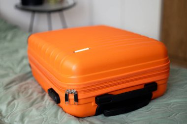 Işık odasındaki yatağın üzerinde büyük turuncu bir bavul. Bagaj bavulu seyahat tatiline hazırlanıyor. Yaşam tarzı, macera ve turizm konsepti.