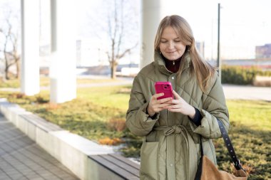 Mutlu kadın telefonda konuşuyor ve dışarıda dinleniyor. Kentsel, halk konsepti. Güneşli bir günde, şehrin sokaklarında gülümseyen bir kadın akıllı telefondan mesaj atıyor.
