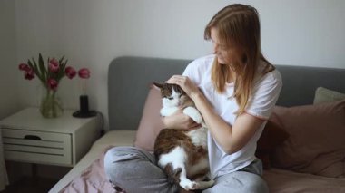 Evde kedisi olan mutlu genç bir kadın. Evcil hayvan dostu kavramı. Sokak kedisi yatakta uyuyor. Rahat ev arka planı, sabah yatma zamanı..