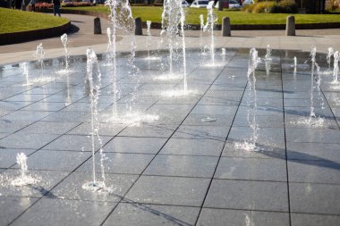 Su damlacıkları havadaki çeşmeden yayıldı. Parktaki fıskiyeden su sıçratmak. Şehir parkındaki meydanda kaldırımda dikey fıskiye fıskiyeleri