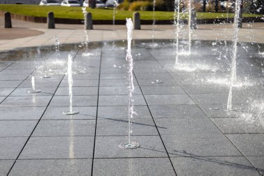 Su damlacıkları havadaki çeşmeden yayıldı. Parktaki fıskiyeden su sıçratmak. Şehir parkındaki meydanda kaldırımda dikey fıskiye fıskiyeleri