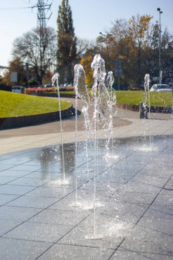 Su damlacıkları havadaki çeşmeden yayıldı. Parktaki fıskiyeden su sıçratmak. Şehir parkındaki meydanda kaldırımda dikey fıskiye fıskiyeleri