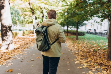 Sonbahar Park Caddesi 'nde sırt çantası takan sarışın genç adam. Şehir yaşam tarzı konsepti. Yüksek kalite fotoğraf