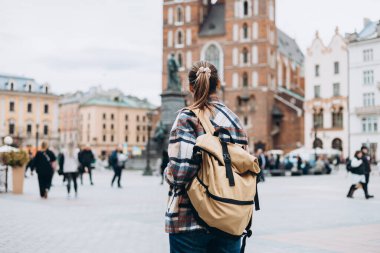 Krakow 'daki Pazar Meydanı' nda sırt çantalı bir turist kadın, sonbaharda Avrupa 'yı geziyor. St. Mary Bazilikası, bulutlu bir gün. Çekici kadın şehri keşfediyor. En iyi turistik yer..