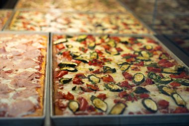 Restoran vitrininde otantik İtalyan pizzası. Cam vitrinli çeşitli pizzacılar. Biberli pizzaya odaklan.